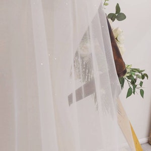 May include: White sheer fabric with a sparkly texture draped over a wooden frame. The fabric is translucent and has a delicate, flowing appearance.