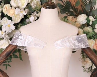 May include: White off-the-shoulder lace bridal bolero with floral embroidery on a white mannequin.
