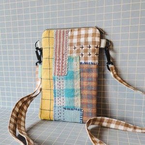 Könnte beinhalten: Eine Patchwork-Handyhülle mit einem braunen und weißen Gingham-Gurt. Die Hülle besteht aus verschiedenen Stoffen in verschiedenen Farben mit einem gelben Hintergrund.