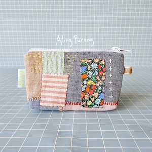 Op de afbeelding: Een patchwork stoffen ritszakje met een bloemenprint, bruine, blauwe en witte strepen en de tekst "Aling Purang" in wit.