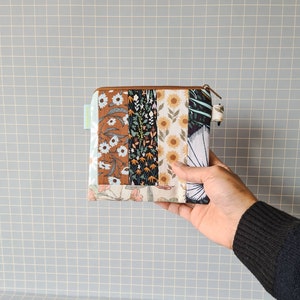 Peut inclure: Une petite pochette zippée avec un motif patchwork composé de motifs floraux et géométriques dans des tons de brun, blanc, vert et bleu.