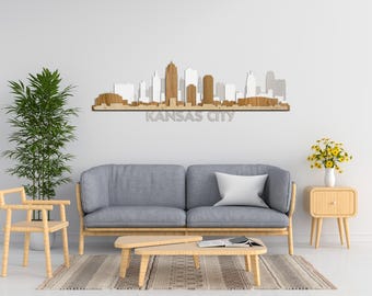 May include: A wooden wall art piece depicting the Kansas City skyline. The art is mounted on a white wall above a gray sofa with a white pillow. The sofa is in front of a light brown rug. There is a small wooden side table to the right of the sofa and a small wooden chair to the left of the sofa. There is a potted plant to the left of the sofa and a vase of yellow flowers on the side table.