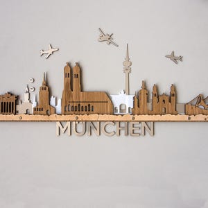 May include: Wooden wall art depicting the Munich skyline with the text "MUNICH" below. The skyline includes buildings, a church, and airplanes.