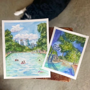 K&ouml;nnte beinhalten: Zwei Aquarellbilder auf Papier. Das linke Bild zeigt ein Schwimmbecken mit Menschen, gr&uuml;nen B&auml;umen und einer Skyline unter blauem Himmel. Das rechte Bild zeigt ein blaues Schild mit der Aufschrift Barton Springs neben B&auml;umen und Wasser.