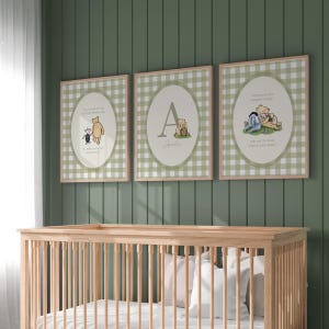 May include: Three rectangular wall art prints featuring a sage green and white gingham pattern background. Each print contains an oval frame with Winnie the Pooh illustrations and text. The centre print displays a large letter A and the name Amelia.