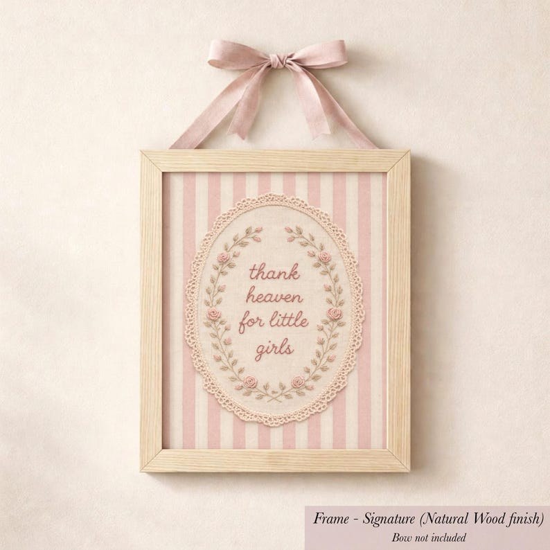 A framed picture with a pink ribbon and lace border, featuring a decorative floral design and the text "Thank heaven for little girls".