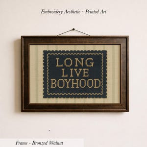 May include: Framed artwork with the text "LONG LIVE BOYHOOD" in a navy blue and tan cross-stitch design. The artwork is in a bronzed walnut frame and is hanging on a white wall. The text "Embroidery Aesthetic - Printed Art" is above the artwork.