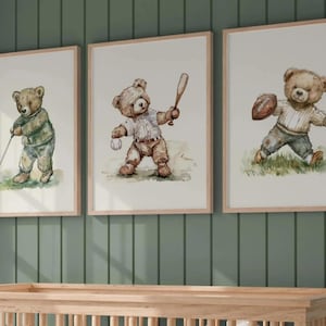 May include: Three framed watercolor prints featuring teddy bears playing sports. One bear golfs, another bats a baseball, and the third holds a football. The prints have light brown wooden frames and are displayed against a green wall.