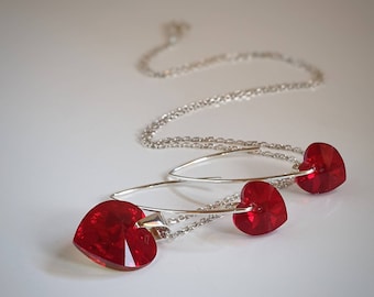 Pode incluir: Um conjunto de colar e brincos de prata com pingentes de cristal vermelho em forma de coração.