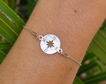 May include: A silver compass bracelet with a circular compass charm featuring a star and the letters N, S, E, and W.