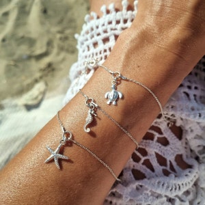 Könnte beinhalten: Drei silberne Charm-Armbänder mit Anhängern zum Thema Ozean. Die Charms umfassen einen Seestern, ein Seepferdchen und eine Schildkröte. Die Armbänder sind filigran und haben ein schlichtes Kettendesign.