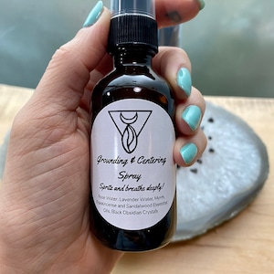 May include: A brown glass bottle with a black spray top and a white label that reads "Grounding & Centering Spray Spritz and breathe deeply! Rose Water, Lavender Water, Myrrh Frankincense and Sandalwood Essential Oils, Black Obsidian Crystals"