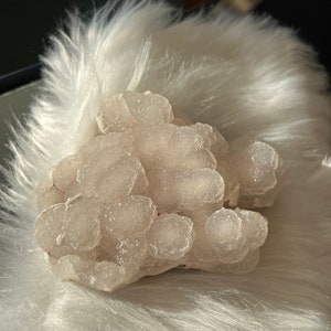 May include: A cluster of white, translucent, round, and slightly bumpy agate stones. The stones are clustered together in a natural formation.