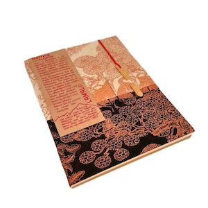 May include: A patterned notebook with a red elastic closure and a wooden bookmark. The cover features a design in shades of orange and black, with text on a tan label. The notebook is designed for writing.