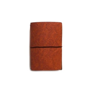 Peut inclure: Un carnet en cuir marron avec une surface texturée et une fermeture à élastique marron.
