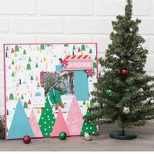 Pu&ograve; includere: Una pagina di scrapbooking rosa e blu con una foto di un bambino che indossa una giacca rosa e blu. La pagina &egrave; decorata con alberi di carta, fiocchi di neve e uno striscione che dice "Joyeux Noel".