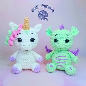 May include: A white crocheted unicorn with a pink flower crown and a light green horn sits next to a light green crocheted dragon with purple wings. Both toys have black eyes and are sitting on a pink surface.