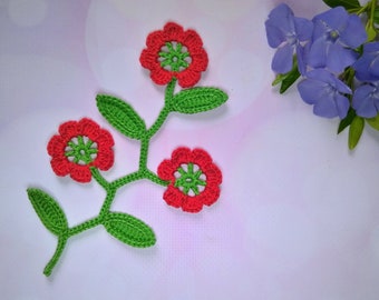 May include: A crocheted flower applique with three red flowers and green leaves. The flowers have a green center.
