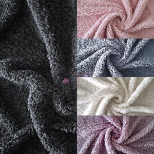 May include: Close-up of five fabric swatches in different colours: dark grey, light pink, dark grey, cream, and light purple. The fabric has a soft, fuzzy texture.