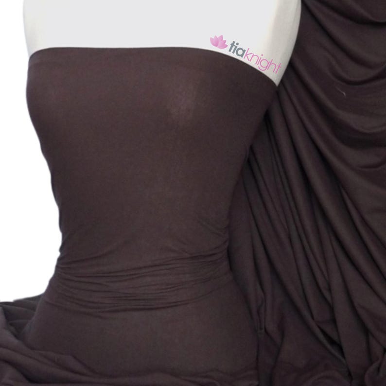 Puede incluir: Primer plano de una tela marr&oacute;n el&aacute;stica. La tela es lisa y tiene un ligero brillo. Est&aacute; drapeada sobre un maniqu&iacute;.