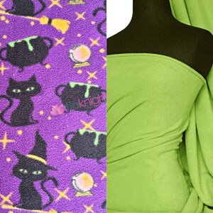 May include: Purple fleece fabric with a black cat, cauldron, and crystal ball Halloween print. A solid green fleece fabric is shown next to the printed fabric.
