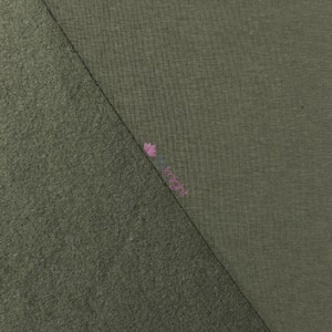 May include: An olive green fabric sample with two distinct textures. One side has a smooth, knit appearance, while the other has a textured, fuzzy surface. The two textures are divided diagonally across the image.