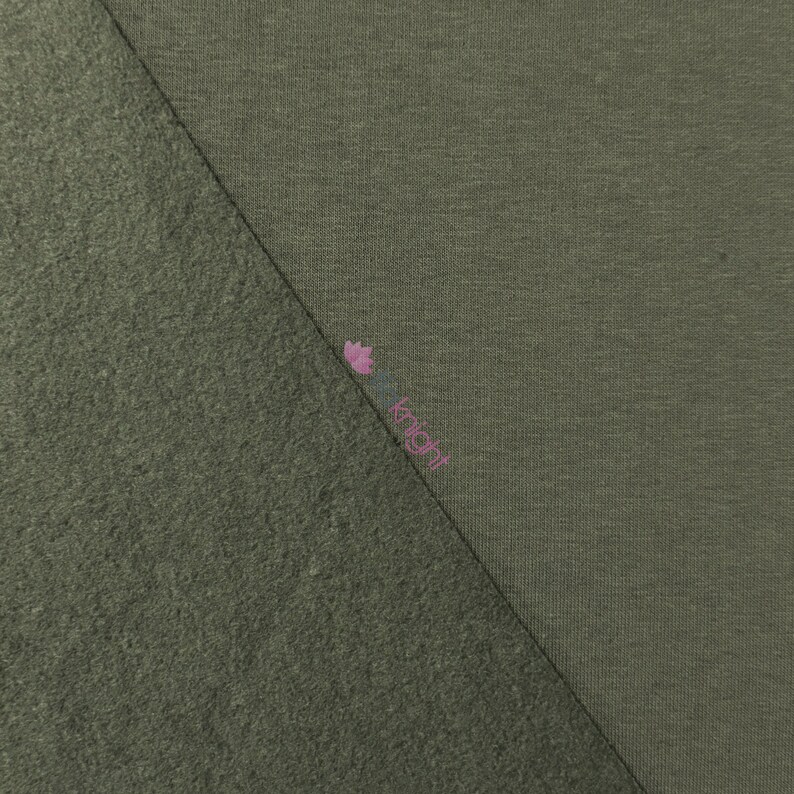 May include: An olive green fabric sample with two distinct textures. One side has a smooth, knit appearance, while the other has a textured, fuzzy surface. The two textures are divided diagonally across the image.