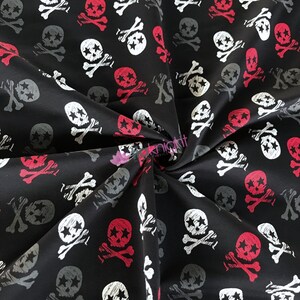 May include: Black fabric with a repeating pattern of white and red skull and crossbones. The skulls have stars in their eyes.