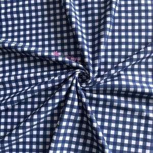 K&ouml;nnte beinhalten: Ein Stoff mit einem klassischen marineblauen und wei&szlig;en Vichy-Karo-Muster. Das Material ist in der Mitte gerafft, wodurch weiche Falten und Drapierungen entstehen. Ein kleines rosa Logo mit dem Text "itaknight" ist auf der Stoffoberfl&auml;che sichtbar.