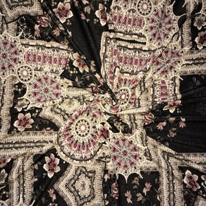May include: Black fabric with a repeating pattern of intricate floral and geometric designs in shades of cream, burgundy, and gold.