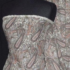 Puede incluir: Una tela blanca con un patrón de paisley en tonos marrones, rosados y grises. La tela es suave y tiene un brillo sutil.