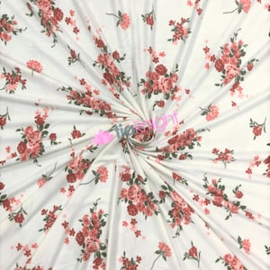 May include: White fabric with a pink and green floral print. The fabric is folded and twisted, showing the pattern.