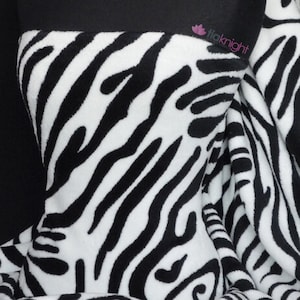May include: Black and white zebra print fleece fabric. The fabric has a soft, fuzzy texture.