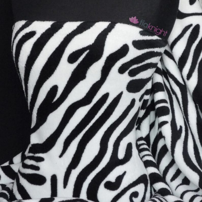 May include: Black and white zebra print fleece fabric. The fabric has a soft, fuzzy texture.