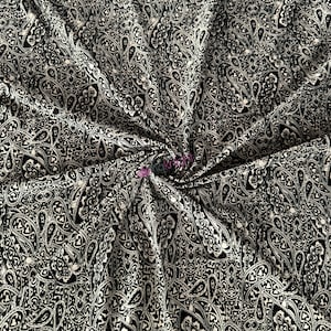 May include: Black fabric with a white paisley pattern. The fabric is wrinkled and has a soft, flowing texture.