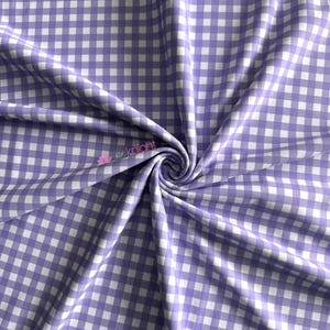 K&ouml;nnte beinhalten: Ein Stoff mit einem klassischen Vichy-Karo-Muster aus abwechselnd hellvioletten und wei&szlig;en Quadraten. Das Material ist zu einem zentralen Wirbel gerafft, wodurch weiche Falten und Drapierungen auf der Oberfl&auml;che entstehen. Der Text "knight" ist in Pink sichtbar.