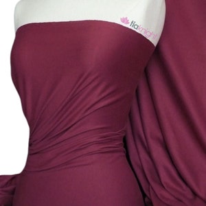 Puede incluir: Primer plano de una tela de color burdeos oscuro, drapeada y doblada para mostrar su textura. La tela es lisa y tiene un ligero brillo.