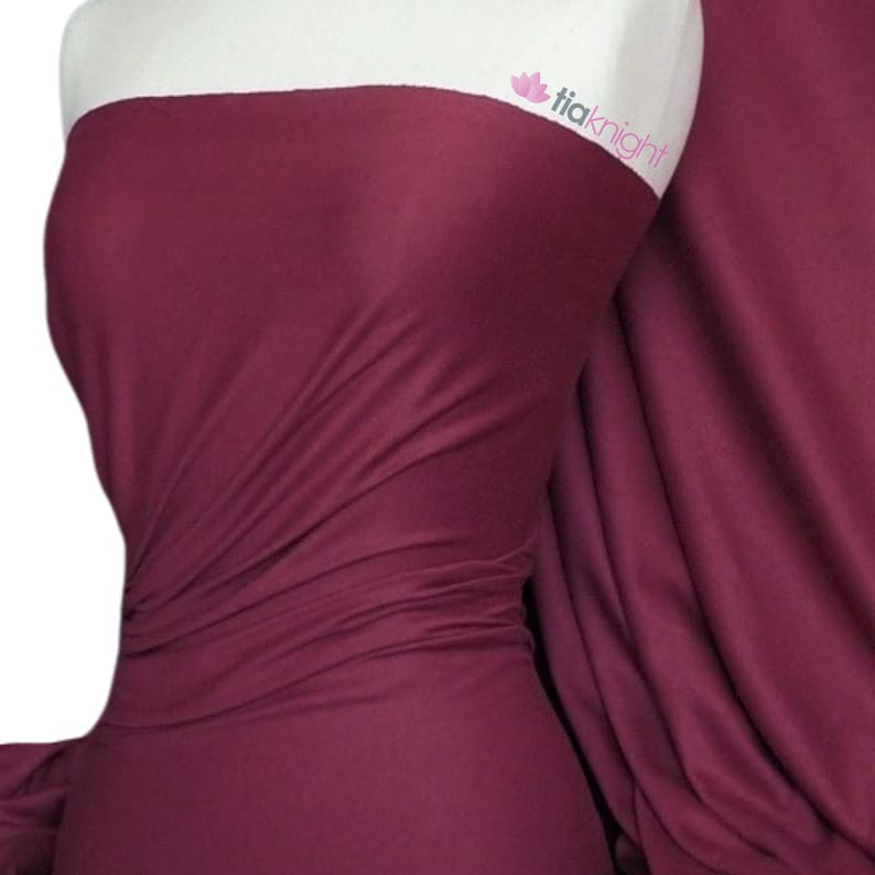 Puede incluir: Primer plano de una tela de color burdeos oscuro, drapeada y doblada para mostrar su textura. La tela es lisa y tiene un ligero brillo.