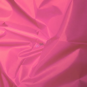 May include: A close-up of a vibrant pink fabric with subtle grid-like texture. The material is gathered and folded, creating shadows and highlights that add depth. The word "tia" is visible in the lower right corner.