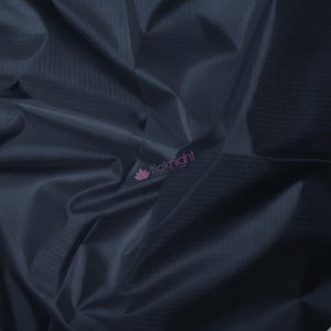 May include: Close-up of navy blue fabric with a subtle grid pattern. The material is folded, creating shadows and highlights that emphasize its texture. The fabric appears smooth and possibly water-resistant, suitable for various crafting projects.