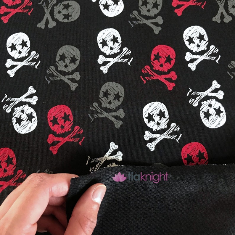 May include: Black fabric with a repeating pattern of white, red, and gray skull and crossbones. The fabric has a slightly textured surface.