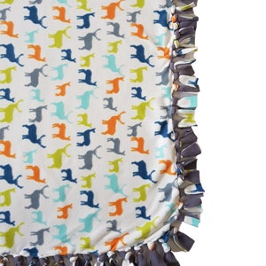 May include: A white fleece blanket with a pattern of colorful reindeer. The blanket has a knotted fringe border in gray, blue, and orange.