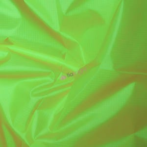 May include: Bright neon green fabric with a subtle grid pattern. The material is folded and draped, creating shadows and highlights that emphasize its texture and sheen. The fabric appears lightweight and possibly synthetic.