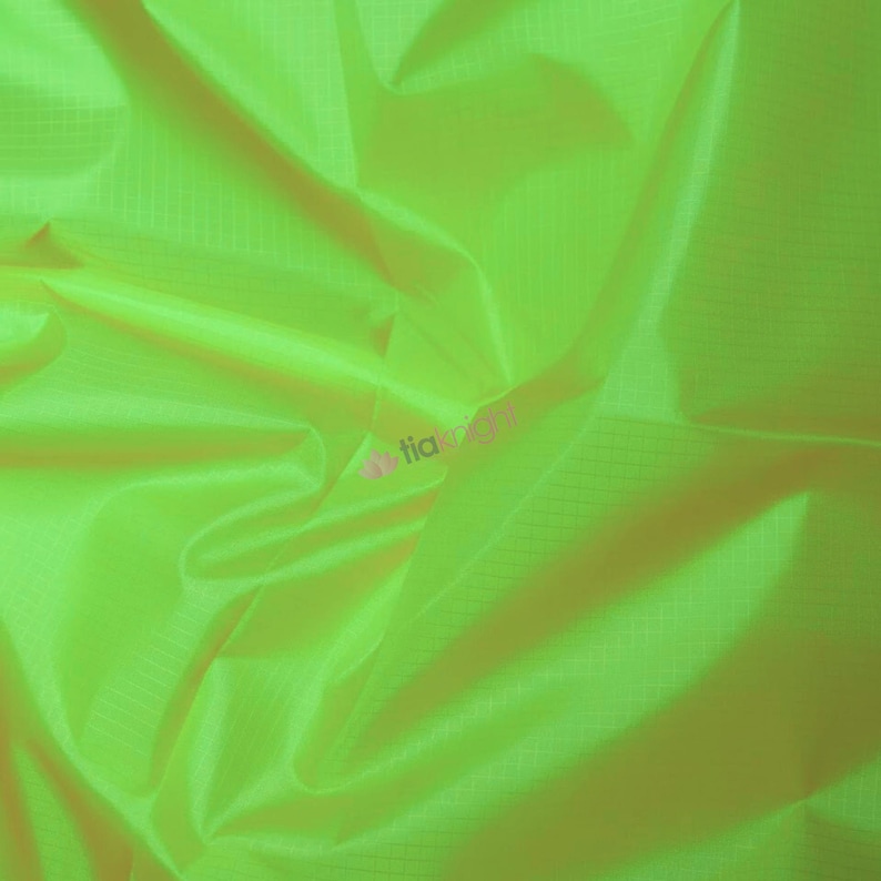 May include: Bright neon green fabric with a subtle grid pattern. The material is folded and draped, creating shadows and highlights that emphasize its texture and sheen. The fabric appears lightweight and possibly synthetic.