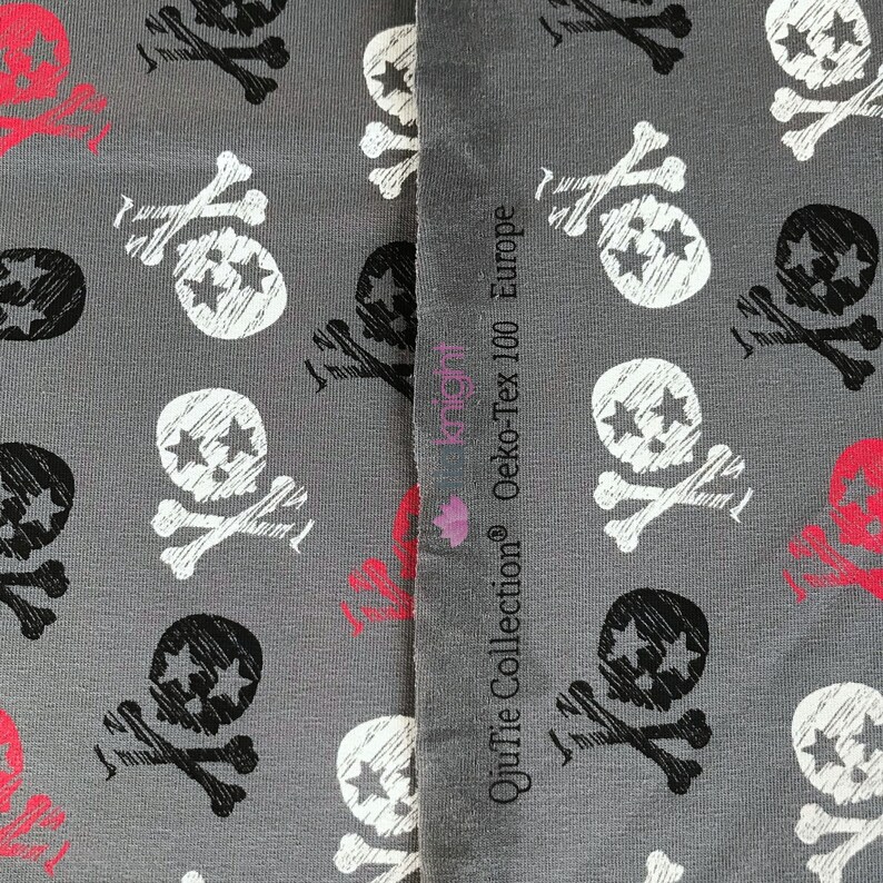 May include: Gray fabric with a repeating pattern of black and white skull and crossbones with stars. The fabric has a label that reads "Quiffie Collection&reg; Oeko-Tex 100 Europe".