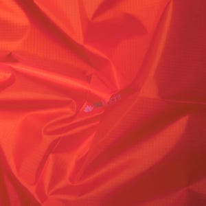 May include: Close-up of vibrant orange fabric with a subtle grid pattern. The material is heavily wrinkled, creating shadows and highlights that emphasize its texture. The fabric appears lightweight and possibly synthetic.