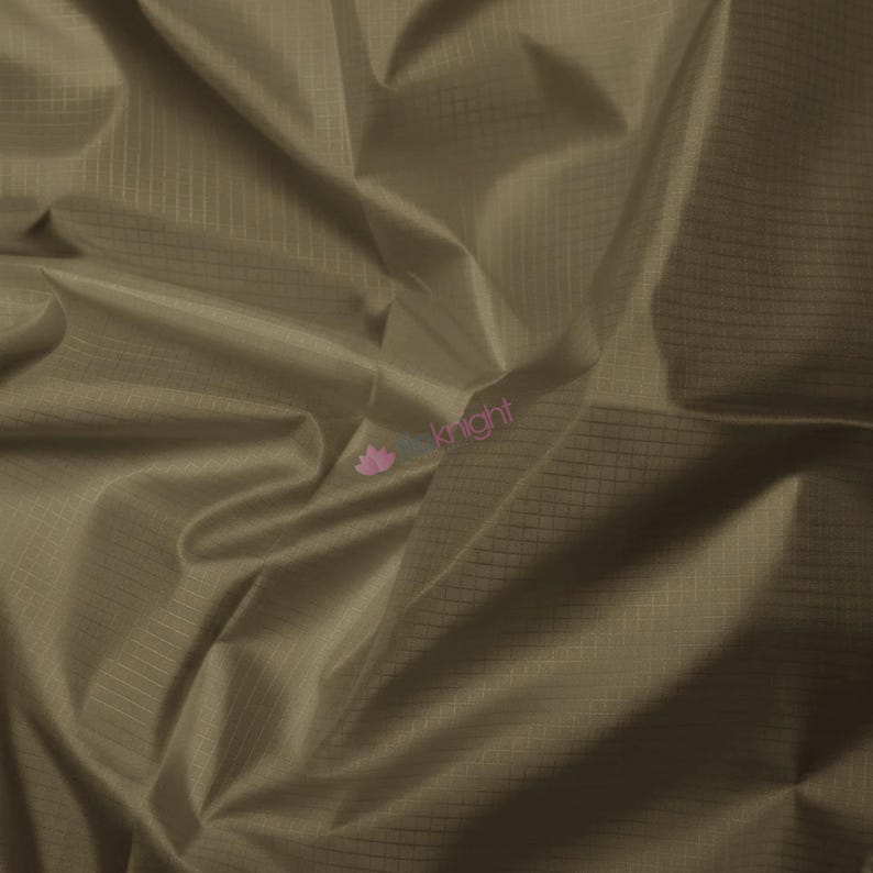 May include: Close-up of a folded, olive-green fabric with a subtle grid pattern. The fabric has a slight sheen, and the folds create shadows and highlights. The material appears lightweight and possibly water-resistant, suitable for various crafting projects.