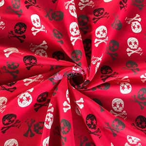 May include: Red fabric with a white and black skull and crossbones pattern. The fabric is folded and the pattern is repeated throughout the fabric.