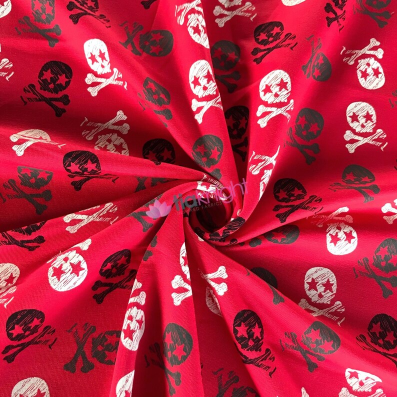 May include: Red fabric with a white and black skull and crossbones pattern. The fabric is folded and the pattern is repeated throughout the fabric.