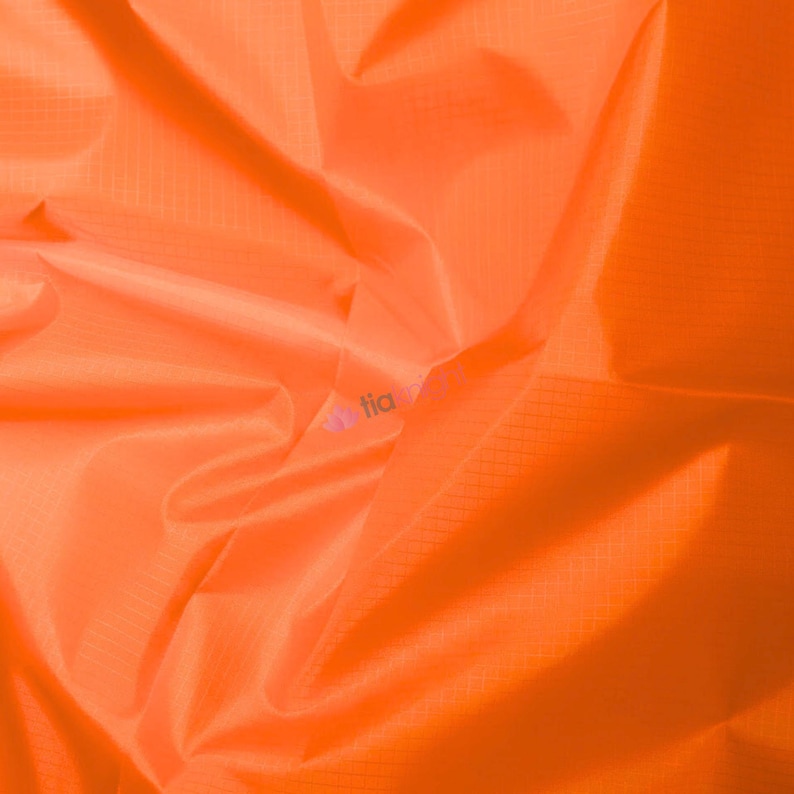 May include: Bright orange fabric with a subtle grid pattern. The material is tightly woven and appears to be lightweight, with soft folds and creases. The fabric has a smooth, slightly shiny surface.